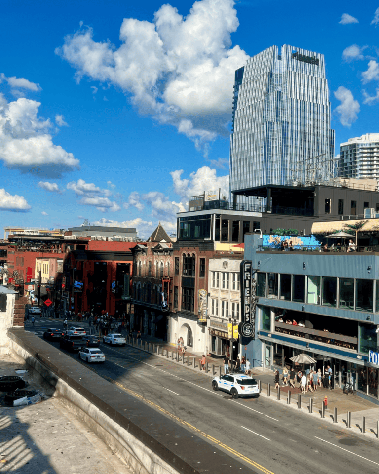 Rooftop view over Lower Broadway in Nashville with honky tonk bars, neon signs, and the Pinnacle tower.