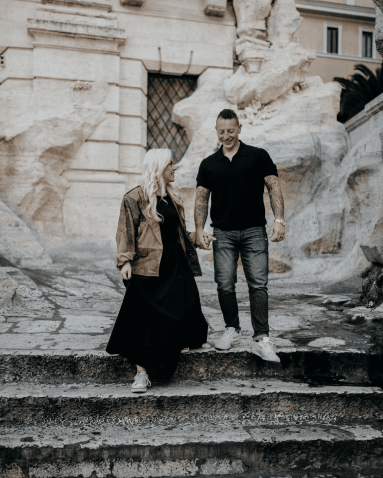Couple holding hands on the steps of the Trevi Fountain in Rome at sunrise, before the crowds arrive.