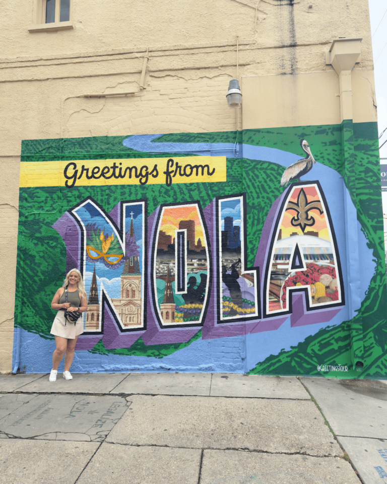 Woman posing in front of the Greetings from NOLA postcard mural in New Orleans, a popular photo spot.