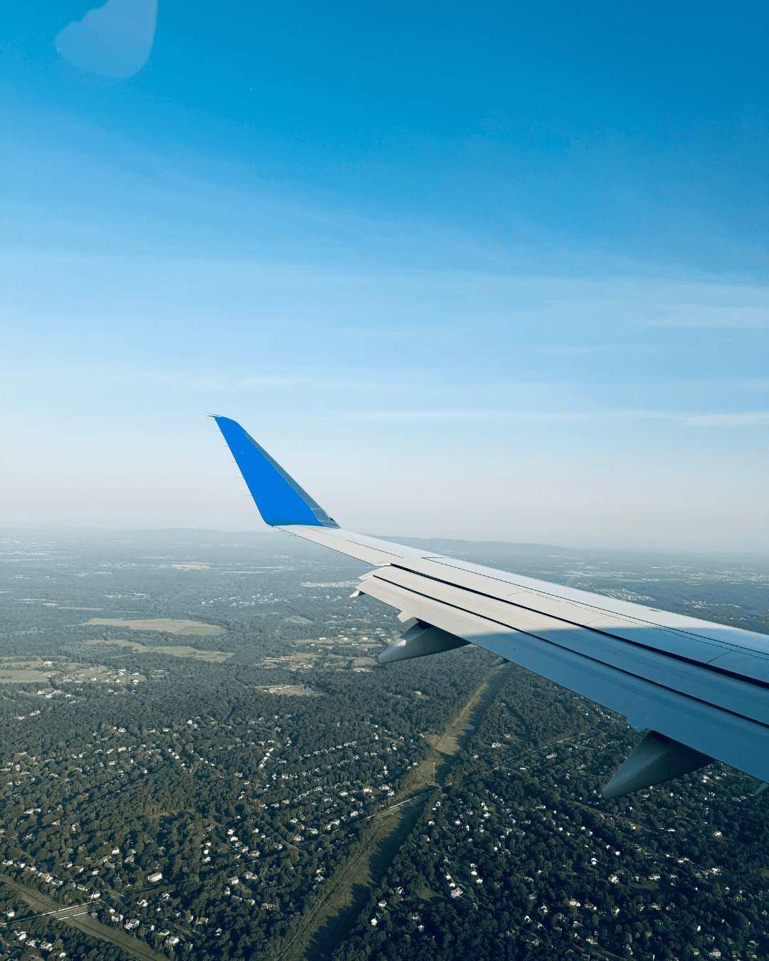 View of an airplane wing over green countryside, illustrating travel safety tips for couples flying abroad