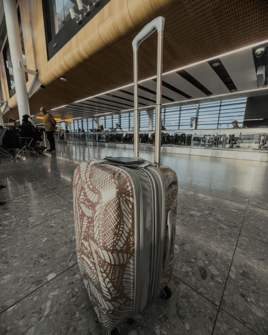 Carry-on suitcase with a passport on top in an airport terminal, ready for an international trip and eSIM setup.