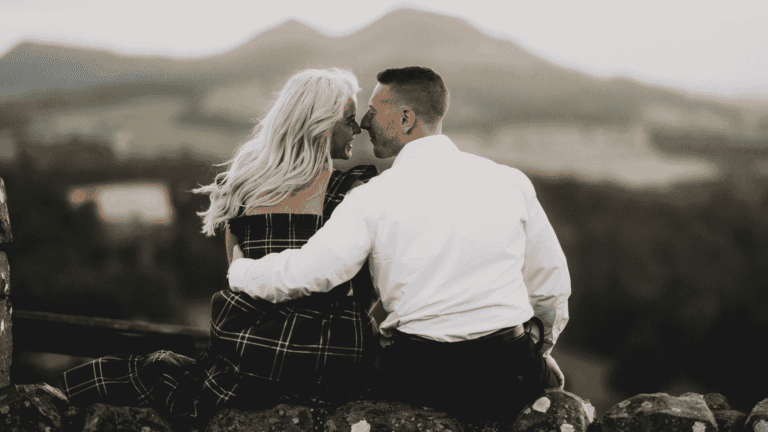A couple sits closely on a stone wall overlooking a serene landscape — couples travel tips for traveling together without losing the romance.