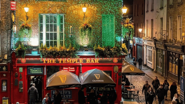 A vibrant night scene of The Temple Bar in Dublin, decorated with green fairy lights and lush greenery. People walk by on a cobblestone street.