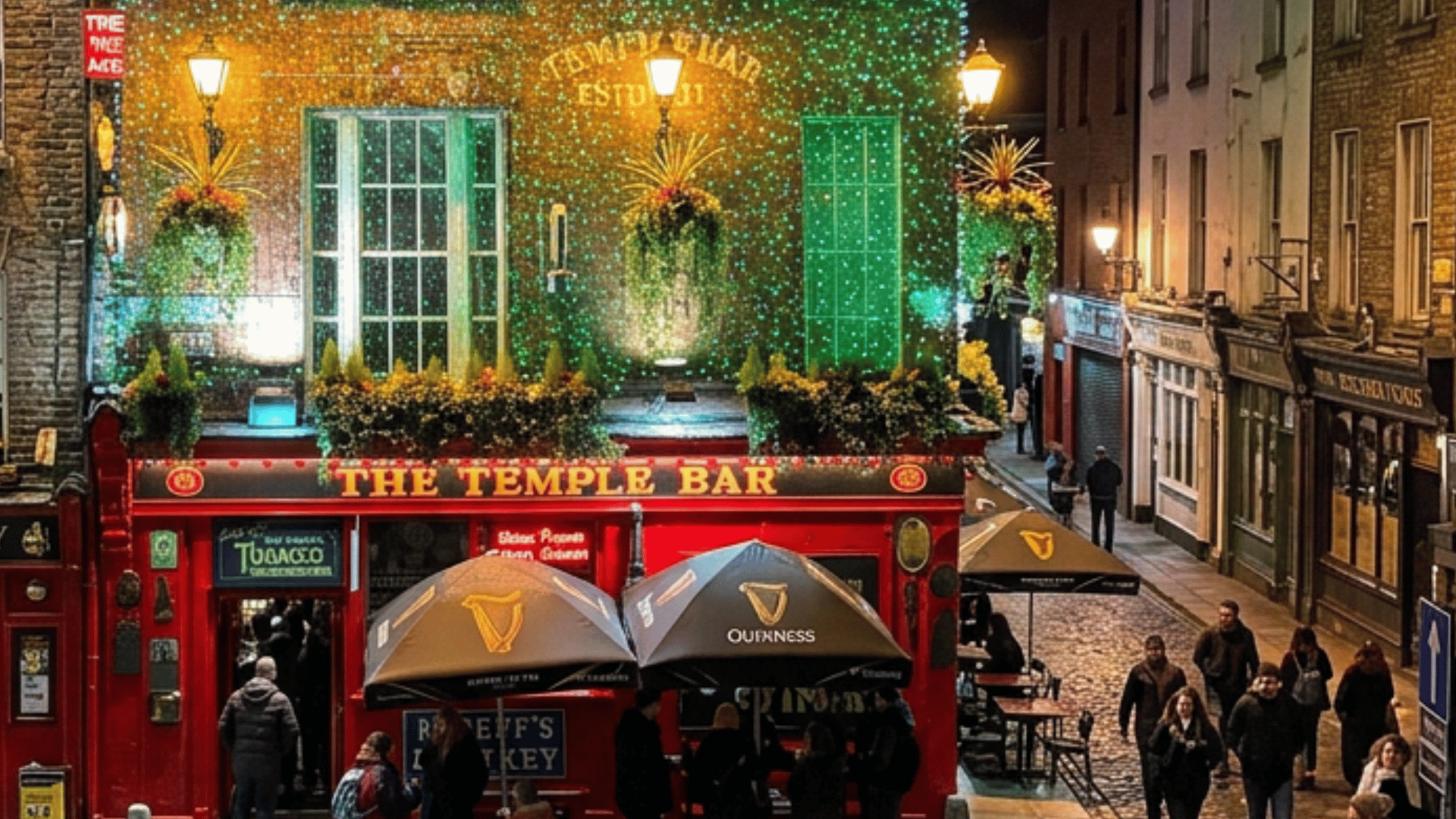 A vibrant night scene of The Temple Bar in Dublin, decorated with green fairy lights and lush greenery. People walk by on a cobblestone street.