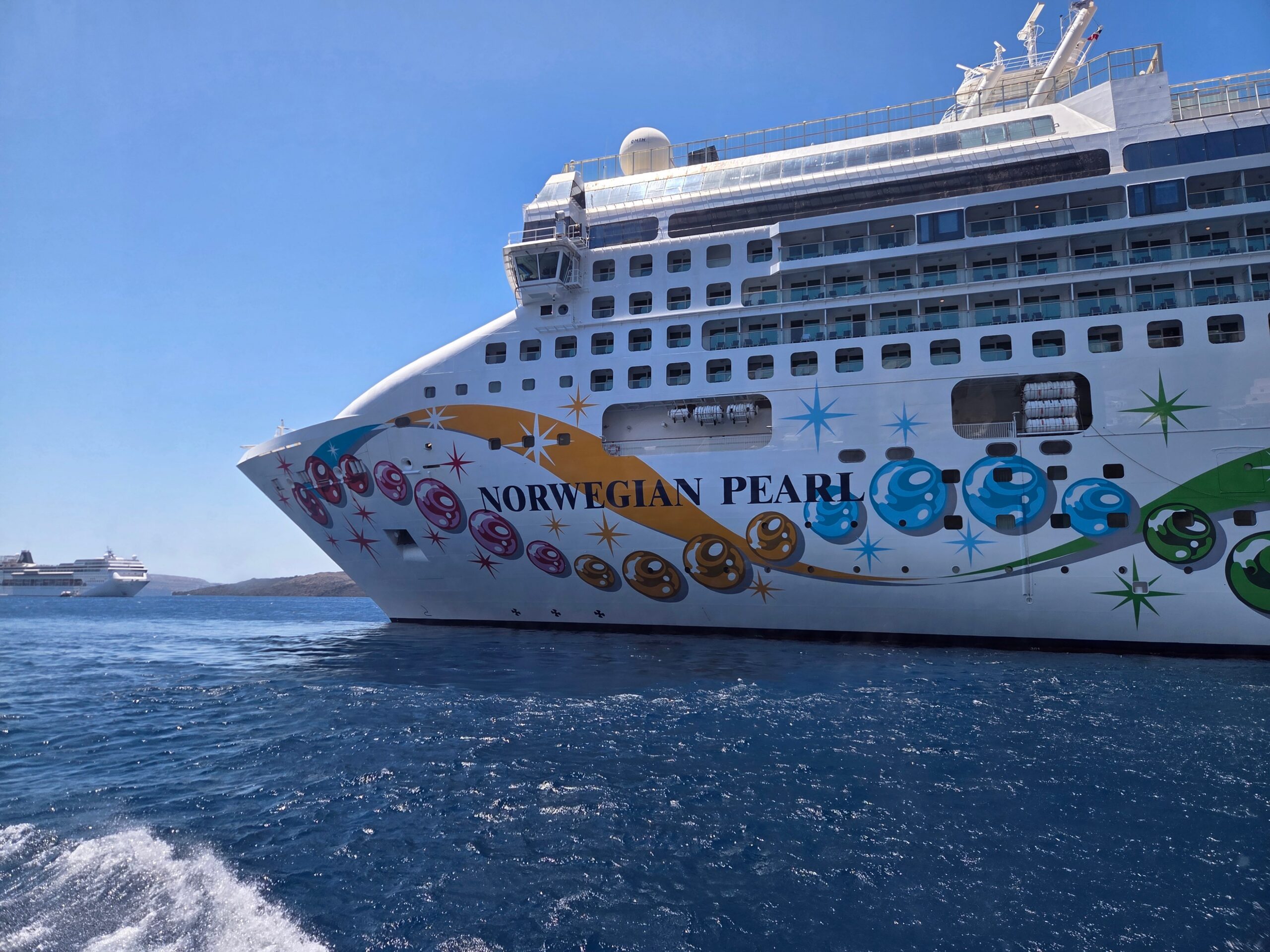 Norwegian Pearl cruise ship decorated with colorful circles and stars, sailing in bright blue water under a clear sky, from our honest cruise packing list.