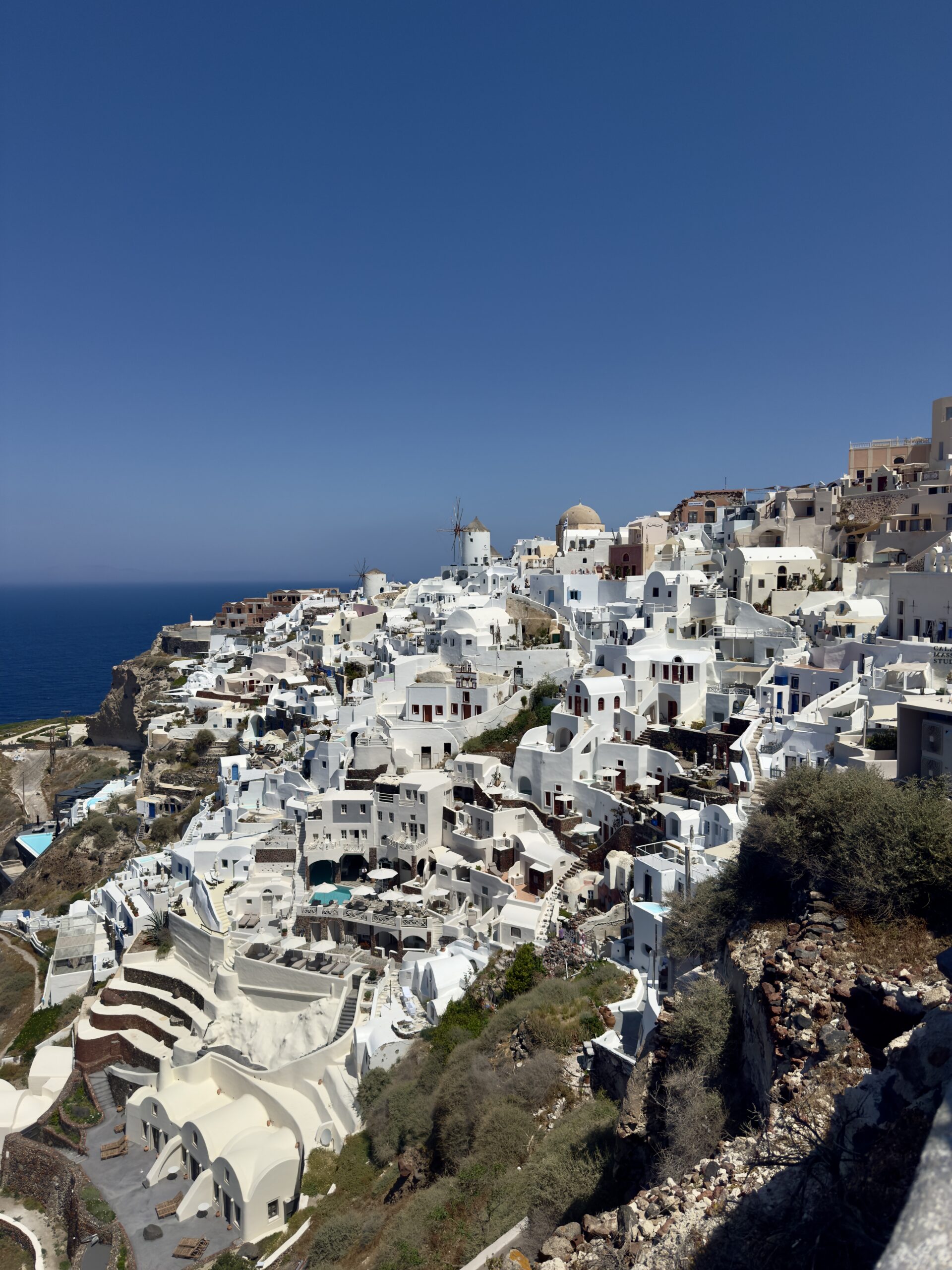 Cliffside view of Santorini, Greece, showcasing iconic white-washed buildings with blue domes against a vibrant blue sky and sea.
