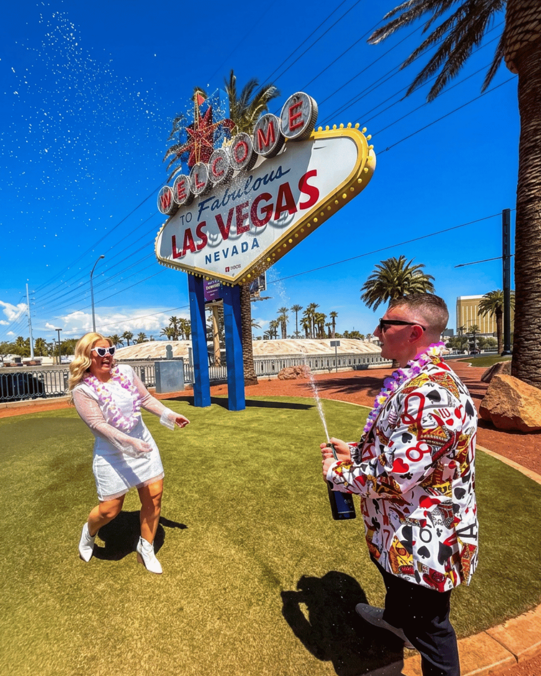 Courtney and Nick spraying champagne at the Welcome to Fabulous Las Vegas sign after their Elvis wedding ceremony