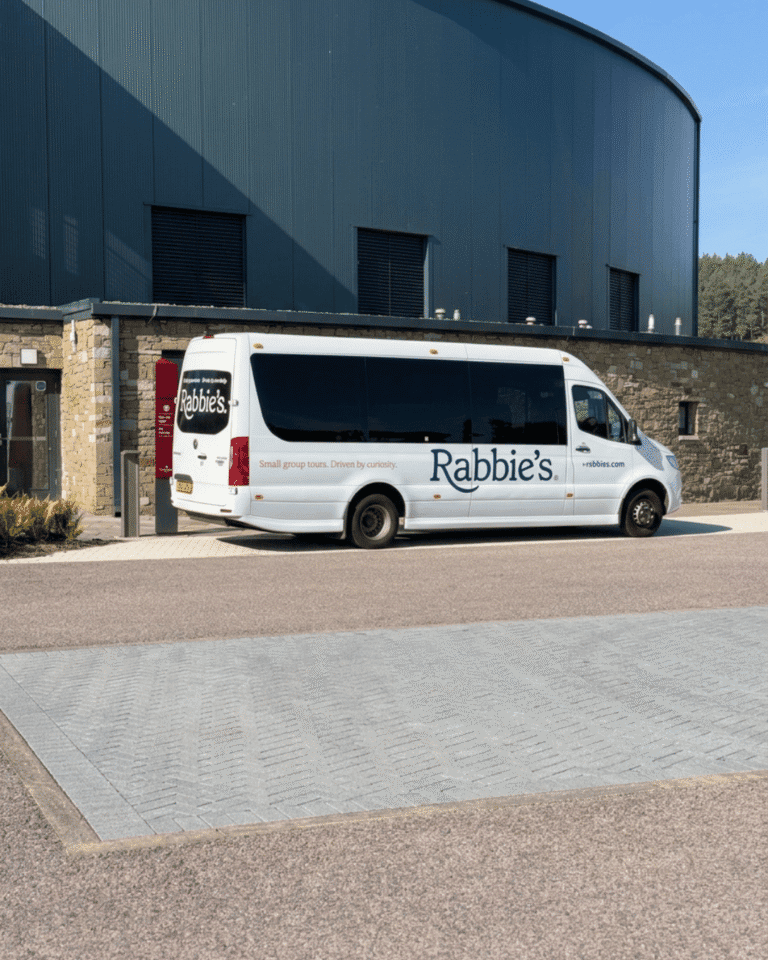 Rabbie's white 16-seat mini coach parked outside a distillery visitor centre on a small group tour in Scotland