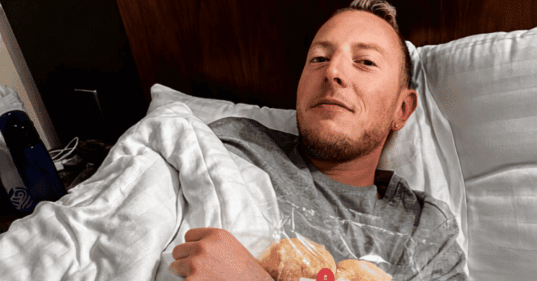 Nick sick in bed in a hotel room in Inverness, Scotland, holding a bag of bread rolls under the covers