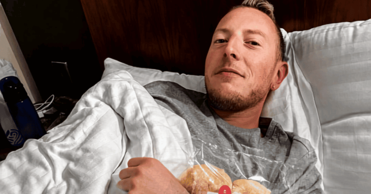 Nick sick in bed in a hotel room in Inverness, Scotland, holding a bag of bread rolls under the covers