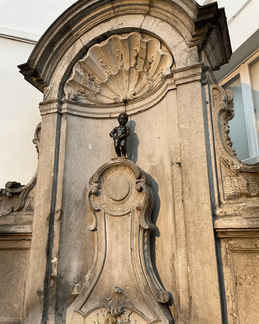 Manneken Pis bronze statue in its carved stone fountain in Brussels